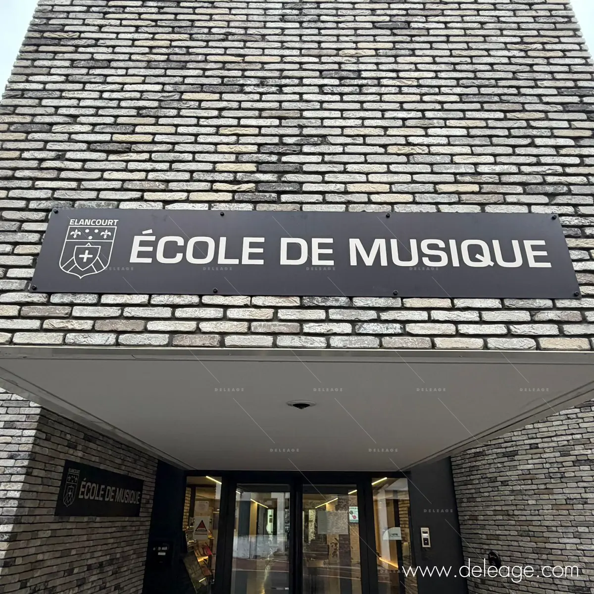 1-enseigne-en-relief-elancourt Enseigne avec logo et lettrage blanc sur fond noir à l'entrée de l'école.
